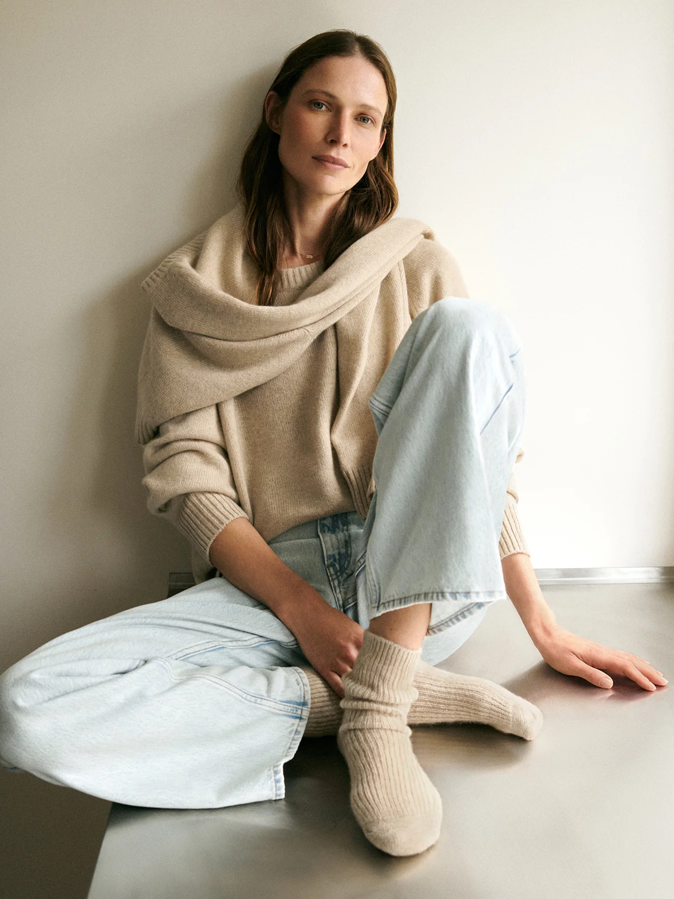 modelka ubrana w kaszmirowy beżowy sweter oraz skarpetki siedząca na metalowym blacie