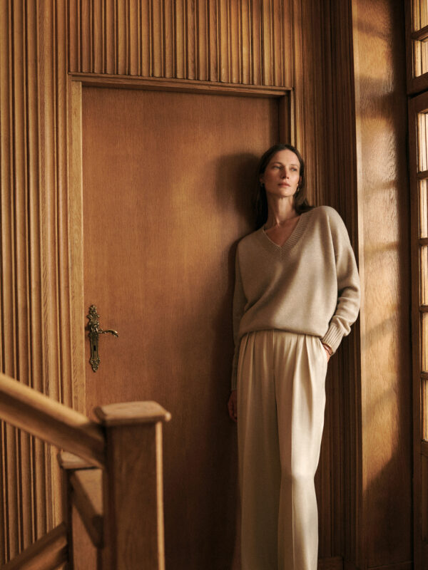 modelka w kaszmirowym beżowym swetrze w serek na tle ściany obitej drewnianą boazerią